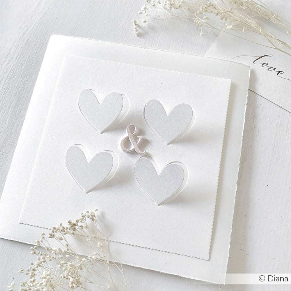 Vier weiße Papierherzen und ein gestanztes kaufmännisches Und-Zeichen von Alexandra Renke auf einer quadratischen Karte, die mit Designpapieren, zarten Trockenblumen und einer herzlichen Liebeserklärung gestaltet wurde.