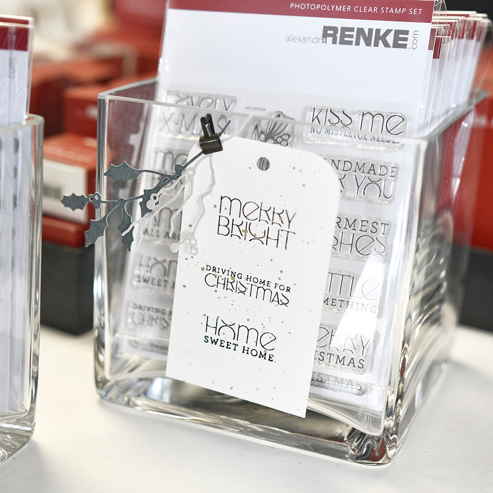 Ein Glasbehälter von Alexandra Renke enthält weihnachtliche Photopolymer-Stempel und einen Anhänger "Merry Bright Home Sweet Home" - ideal für festliche Papierprojekte.