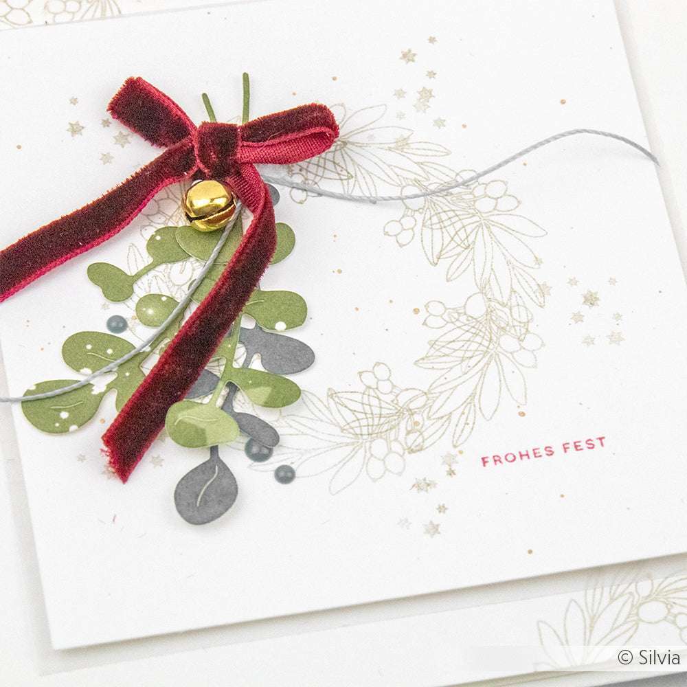 Handgefertigte Weihnachtskarte von Alexandra Renke mit Blättern, einer roten Samtschleife, einer goldenen Glocke und "Frohes Fest" auf Weiß - perfekt für Papierprojekte und mit hochwertigen Photopolymerstempeln hergestellt.