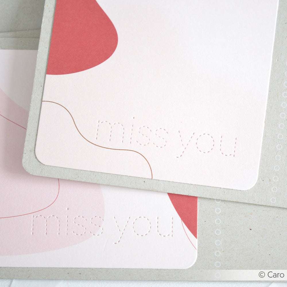 Zwei pastellfarbene Karten von Alexandra Renke mit "Miss you", geprägt mit Stanzformen, die abstrakte rosa und rote Formen zeigen.