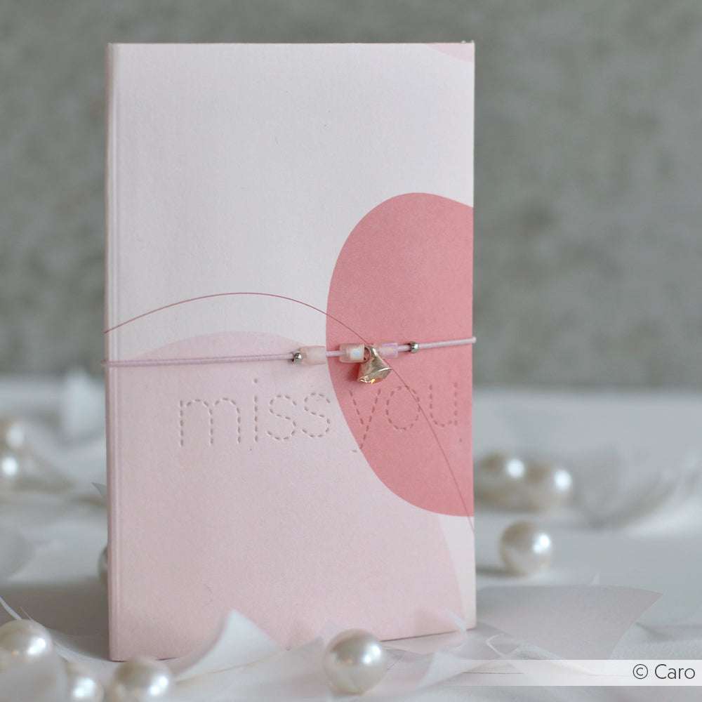 Eine rosafarbene Karte mit dem Text "Ich vermisse dich", gebunden mit einem zarten Bettelarmband und umgeben von Perlen, hergestellt mit den eleganten Stanzen und hochwertigen Designerpapieren von Alexandra Renke.