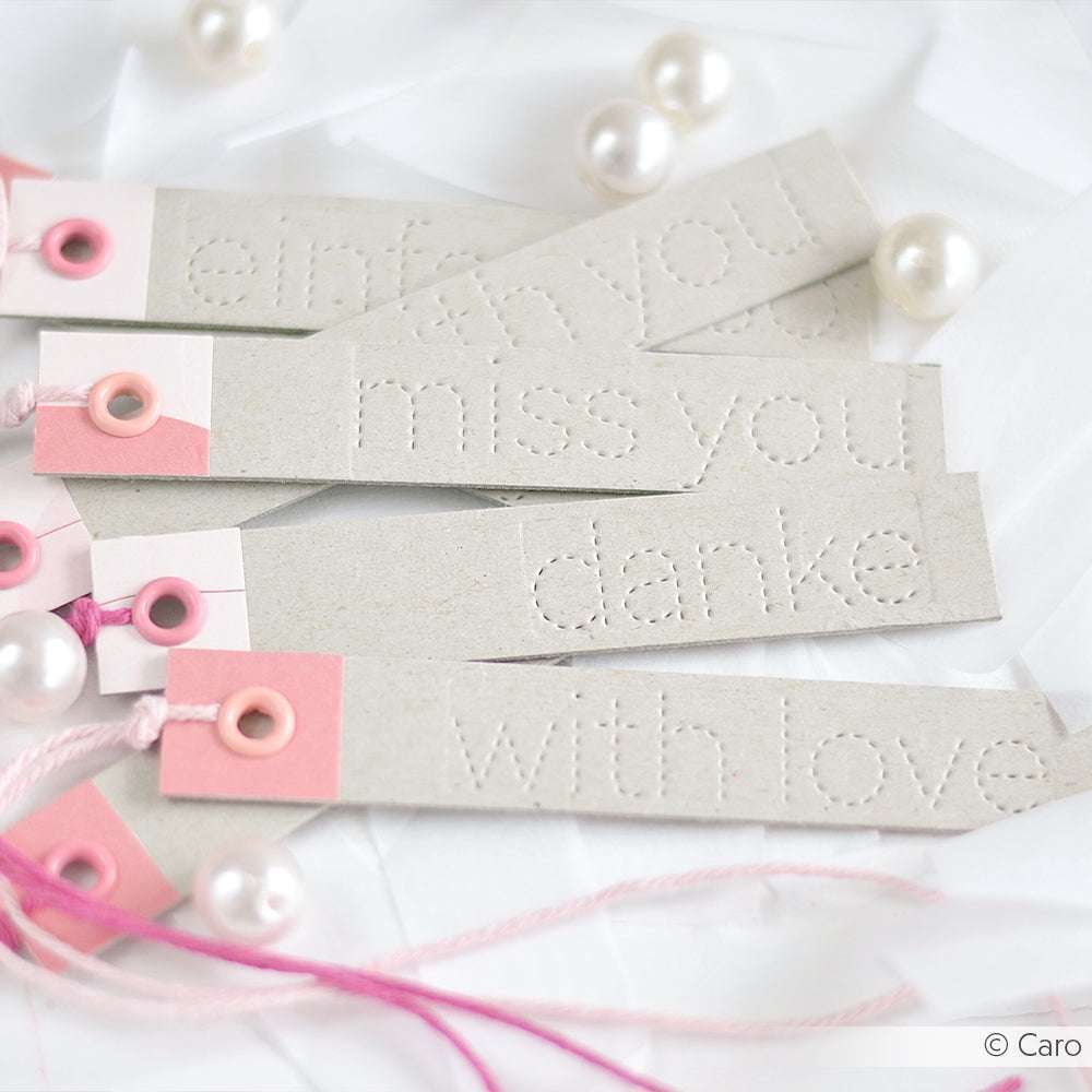 Vier Papieranhänger von Alexandra Renke mit geprägten Botschaften, rosa Akzenten und Perlenverzierungen auf weißem Hintergrund.