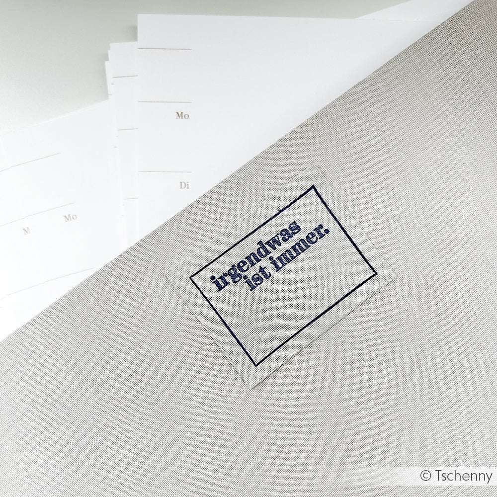 Eine graue Stoffmappe mit der Aufschrift "irgendwas ist immer" von Alexandra Renke liegt auf verstreuten Wochenplanerseiten - eine ideale Inspiration für Ihre Papierprojekte mit den beliebten Clear Stamp Motiven.