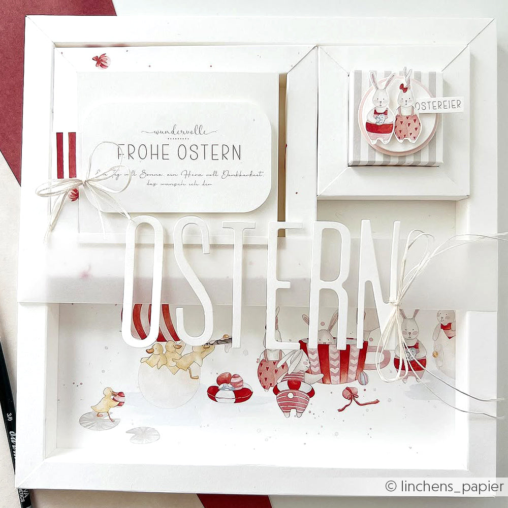 Gerahmte Osterkunst von Alexandra Renke mit "OSTERN"-Ausschnitt, Hasen, Küken, Eiern und einer Karte mit deutschen Wünschen - gestaltet mit Motivstanze Schmales Alphabet und bunten Designpapieren für einen festlichen Touch.