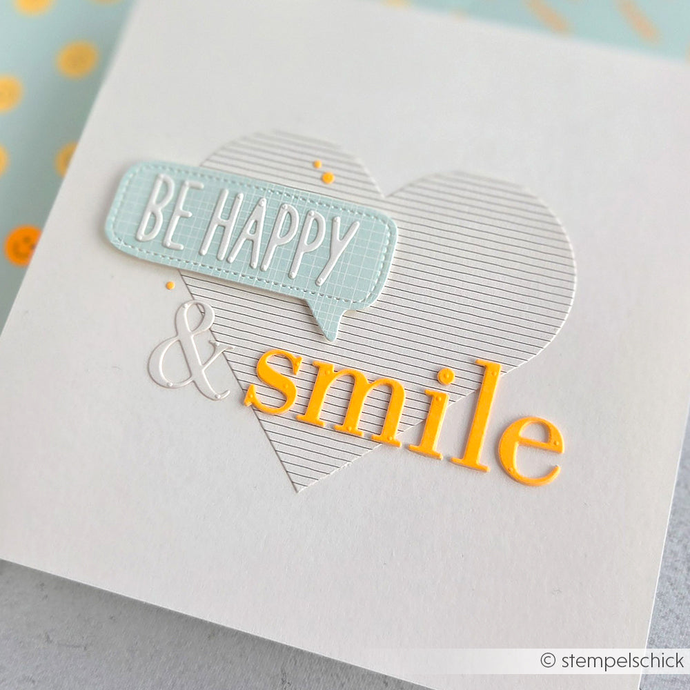Weiße Karte mit einem gestreiften Herz, der Aufschrift „BE HAPPY“ in einer Sprechblase und dem Wort „smile“ in gelben und weißen Buchstaben – gestaltet mit der Motivstanze „Sans Serif Alphabet“ für klare Schriftzüge und veredelt mit passenden Designpapieren. Perfekt für kreative Projekte mit DieCut-Systemen!.