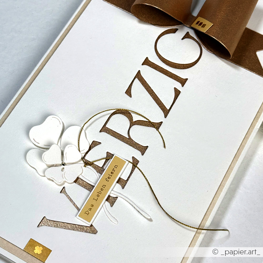 Handgefertigte Karte von Alexandra Renke mit "VIERZIG" in Gold, einer goldenen Schleife, durchsichtigem Kleeblatt und dem Tag "Das Leben feiern" auf weißem Designpapier, hergestellt mit der Motivstanze Alphabet Dezember.