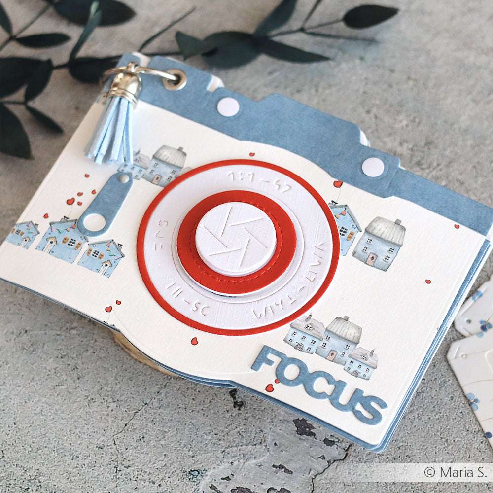 Eine dekorative Karte in Form einer Kamera von Alexandra Renke, hergestellt mit Motivstanze und Designpapieren, mit Häusern, einer Quaste und "FOCUS" auf der Vorderseite.