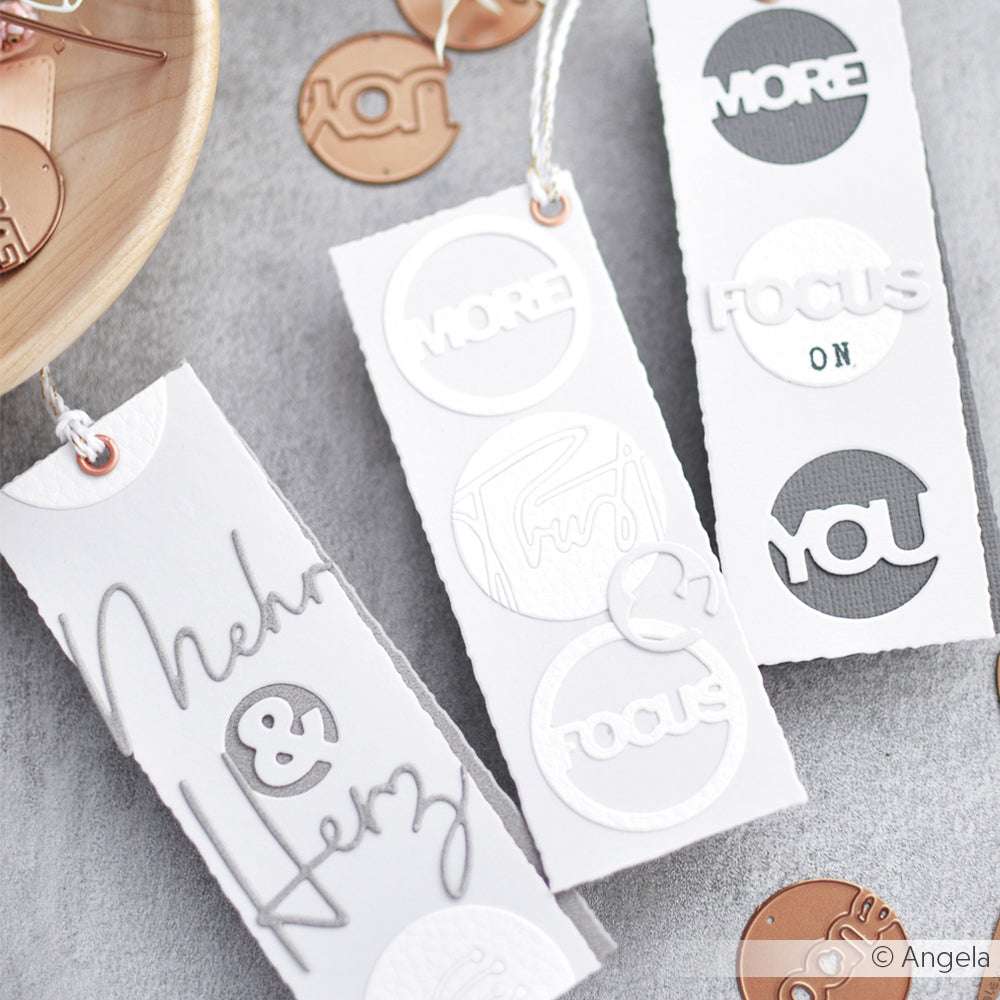 Drei handgefertigte weiße Lesezeichen von Alexandra Renke zeigen geprägte Wörter wie MORE, FOCUS und YOU in einzigartigen Schriftarten, mit Ausschnitten, die mit hochwertigen Stanzen und Stanzsystemen wie der Motivstanze Faith hergestellt wurden.