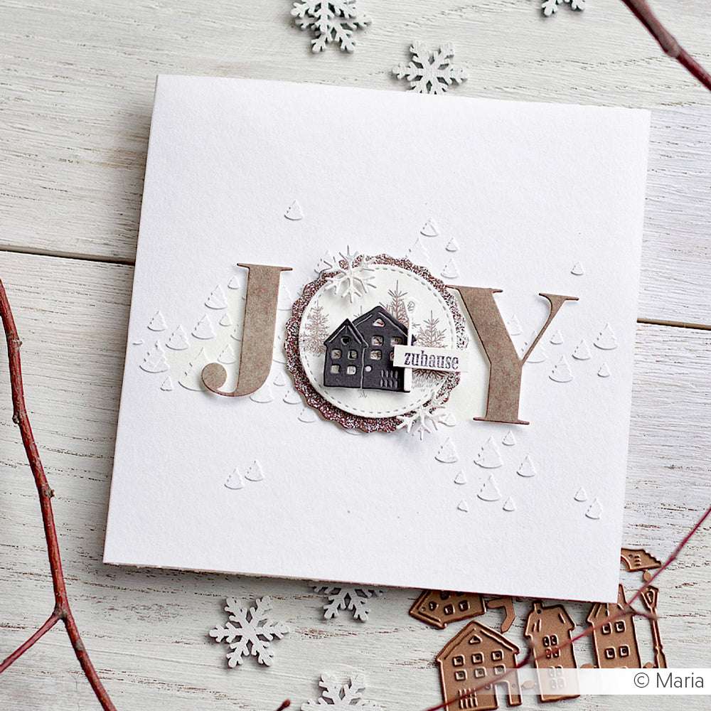 Handgemachte Karte "JOY" mit Alexandra Renke Motivstanze Alphabet Groß, einem Haus, Schneeflocken und strukturierten weißen Details auf einer Holzoberfläche.