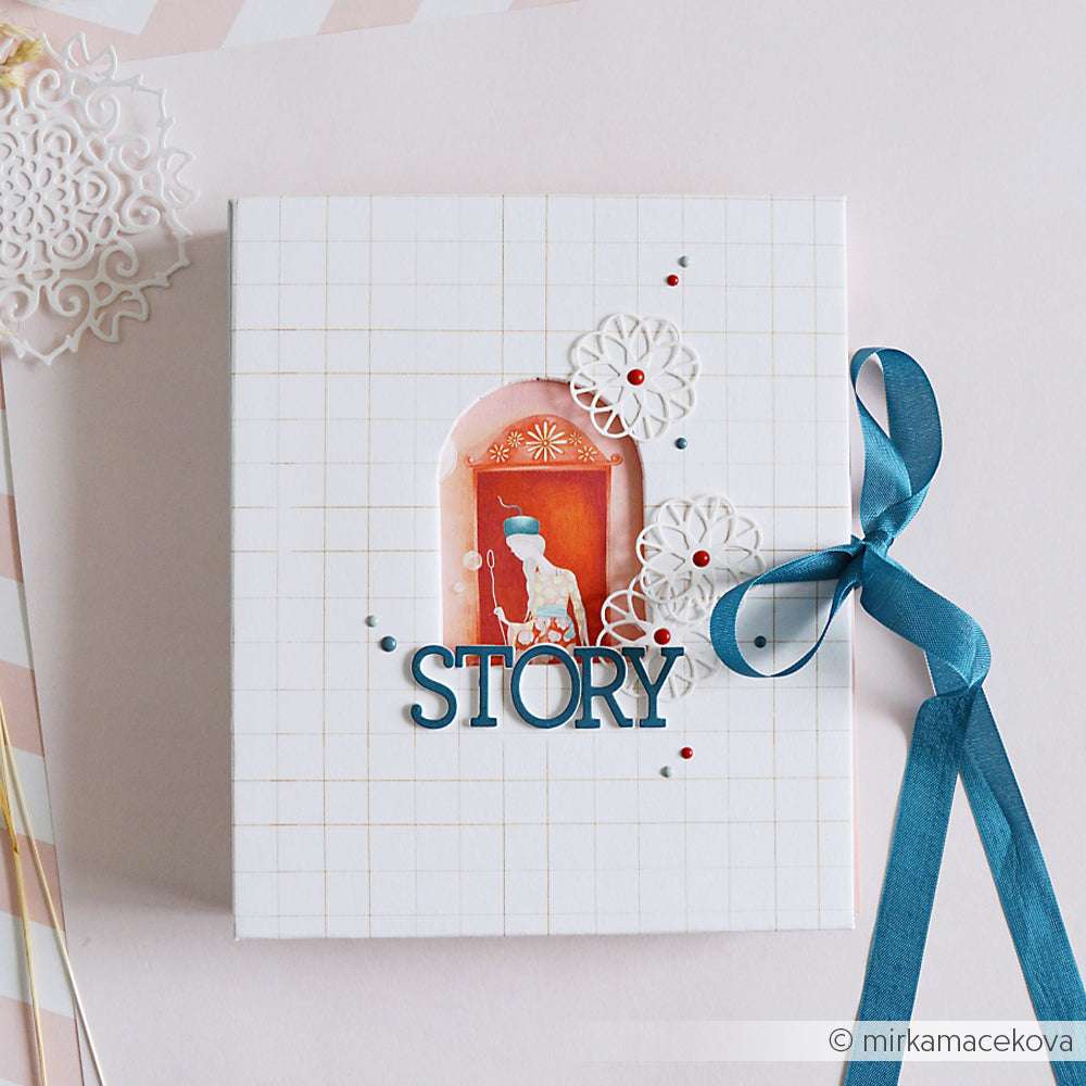 Weißes Scrapbook mit Gittermuster von Alexandra Renke mit blauem Band, Blumenausschnitten, Slab Alphabet Buchstaben und "STORY" auf dem Einband - ideal, um Ihre Lieblingsdesignpapiere und DieCut Systeme zu präsentieren.