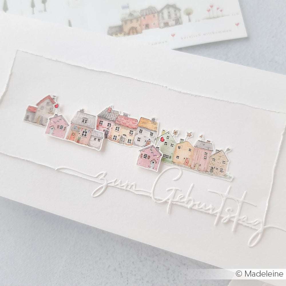 Handgefertigte Geburtstagskarte von Alexandra Renke mit pastellfarbenen Aquarellhäusern, gestaltet mit Motivstanze Zum Geburtstag und hochwertigen Designpapieren, mit eleganter Schrift auf weißem Papier.