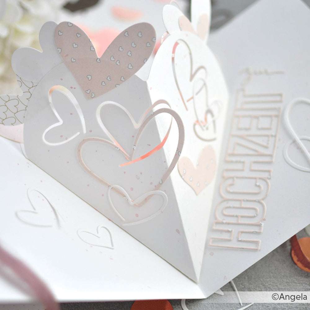 Weiße Pop-up-Hochzeitskarte von Alexandra Renke mit geschichteten Herzmotiven, hergestellt mit DieCut Systemen und mit dem Wort HOCHZEIT in erhabenen Buchstaben.