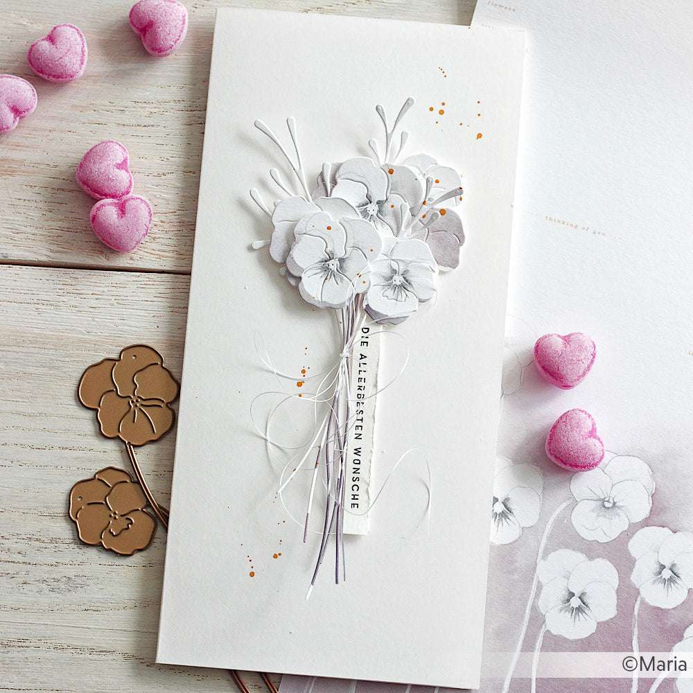 Eine handgefertigte Karte von Alexandra Renke mit Designpapieren und zarten weißen Papierblumen, umgeben von rosafarbenen herzförmigen Verzierungen auf einer weißen Fläche.