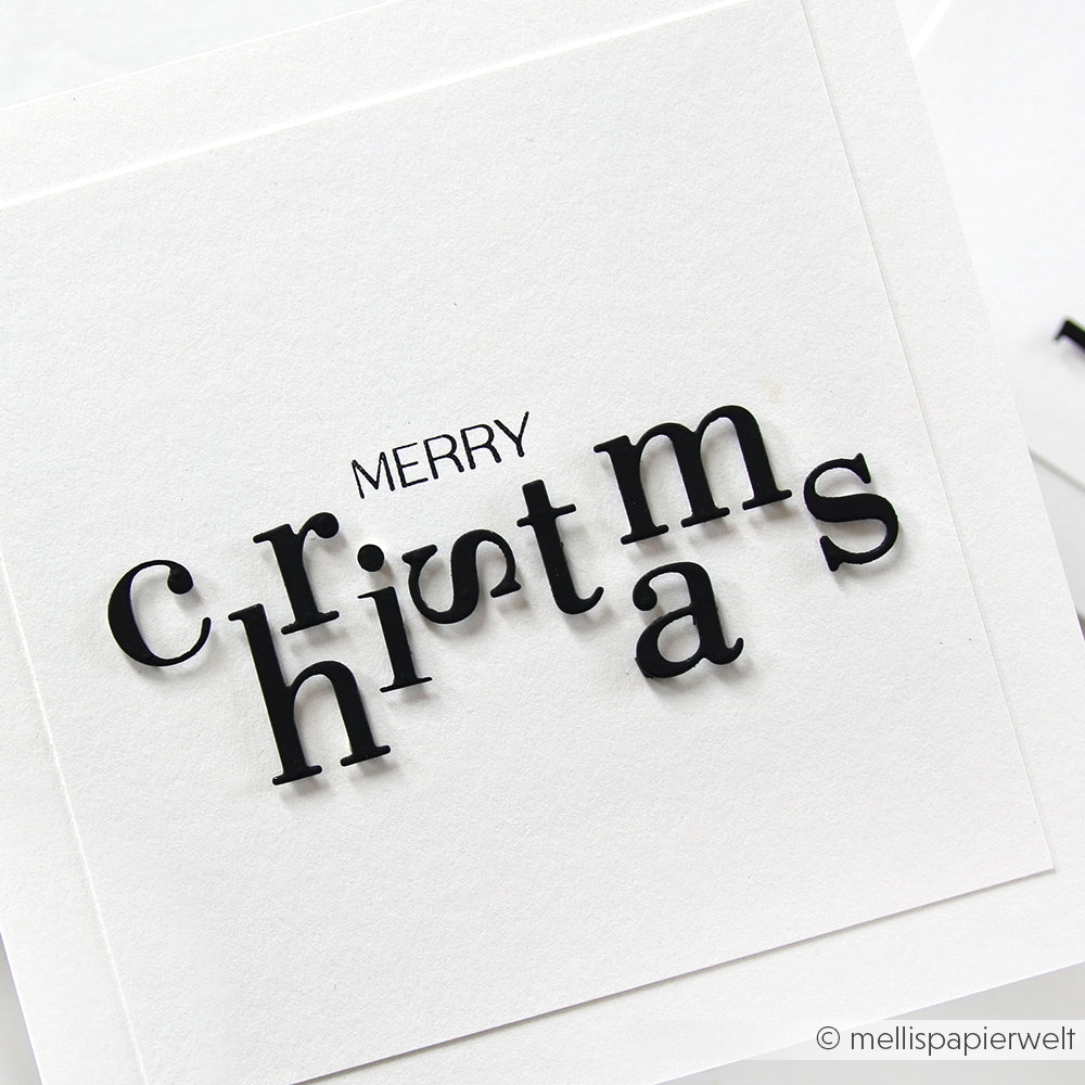 Weiße Karte mit "Frohe Weihnachten" in verspielten, gestaffelten schwarzen Buchstaben auf einfarbigem Hintergrund, gestaltet mit Alexandra Renke Motivstanze Serifbuchstaben für einen einzigartigen und festlichen Touch.