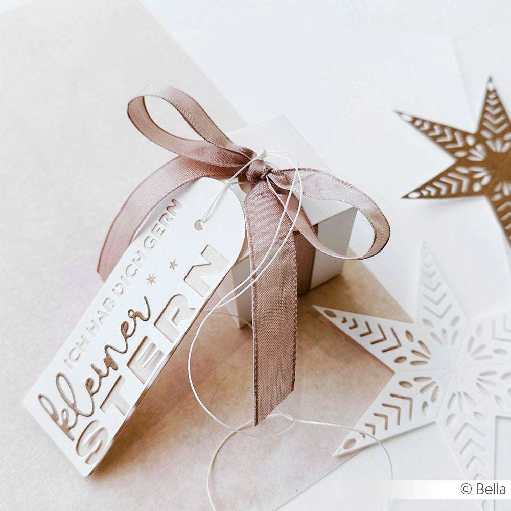 Eine kleine weiße Geschenkschachtel von Alexandra Renke ist mit einem taupefarbenen Band, Sterndekorationen aus Motivstanze und einem Anhänger mit der Aufschrift "kleiner Stern" versehen.