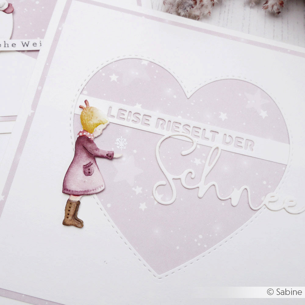 Eine Winterkarte von Alexandra Renke mit einem Mädchen in einem rosa Mantel, Herzmotiven und dem Text "Leise rieselt der Schnee", hergestellt aus eleganten Designpapieren für zusätzlichen Charme.