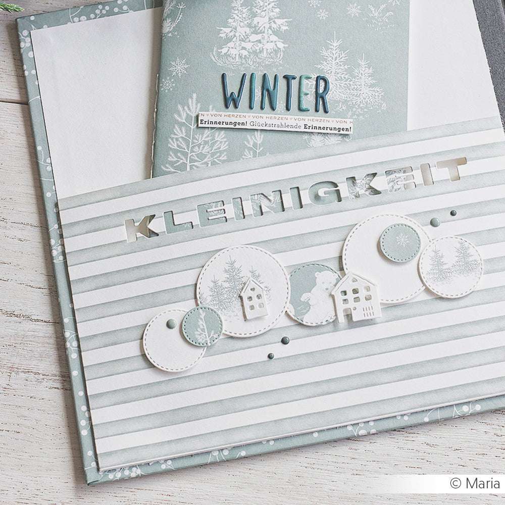 Eine Winterkarte von Alexandra Renke mit KLEINIGKEIT und verschneiten Häusern auf gestreiftem Papier sowie einem Umschlag mit WINTER-Etikett. Hergestellt mit der Motivstanze Kleinigkeit Negativ für zusätzlichen Charme.