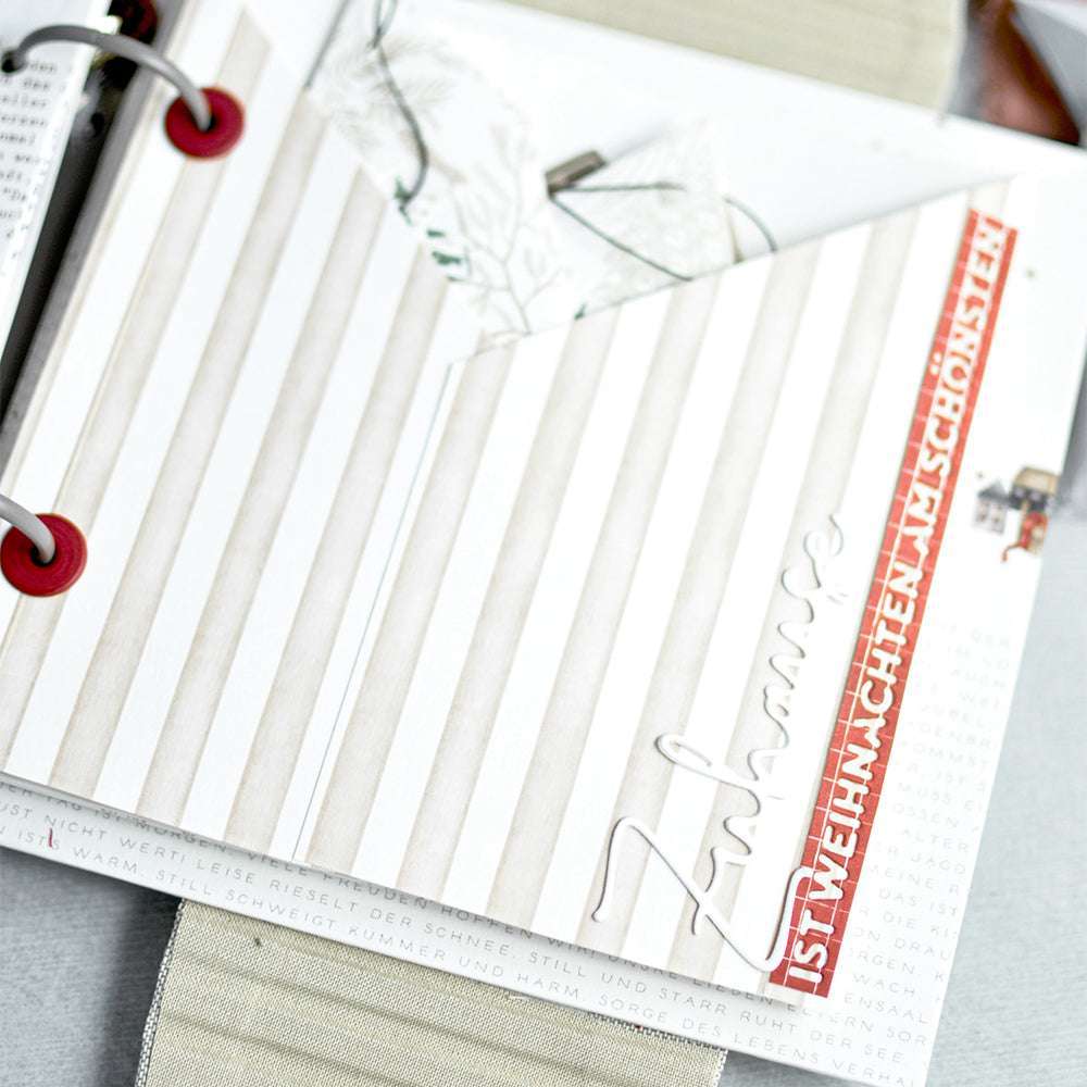 Offenes Scrapbook von Alexandra Renke mit gestreiftem Papier, roten Akzenten und deutschem Text: Zuhause ist Weihnachten am schönsten. Bezaubernde Verzierungen mit einer Motivstanze vervollständigen dieses festliche Layout.