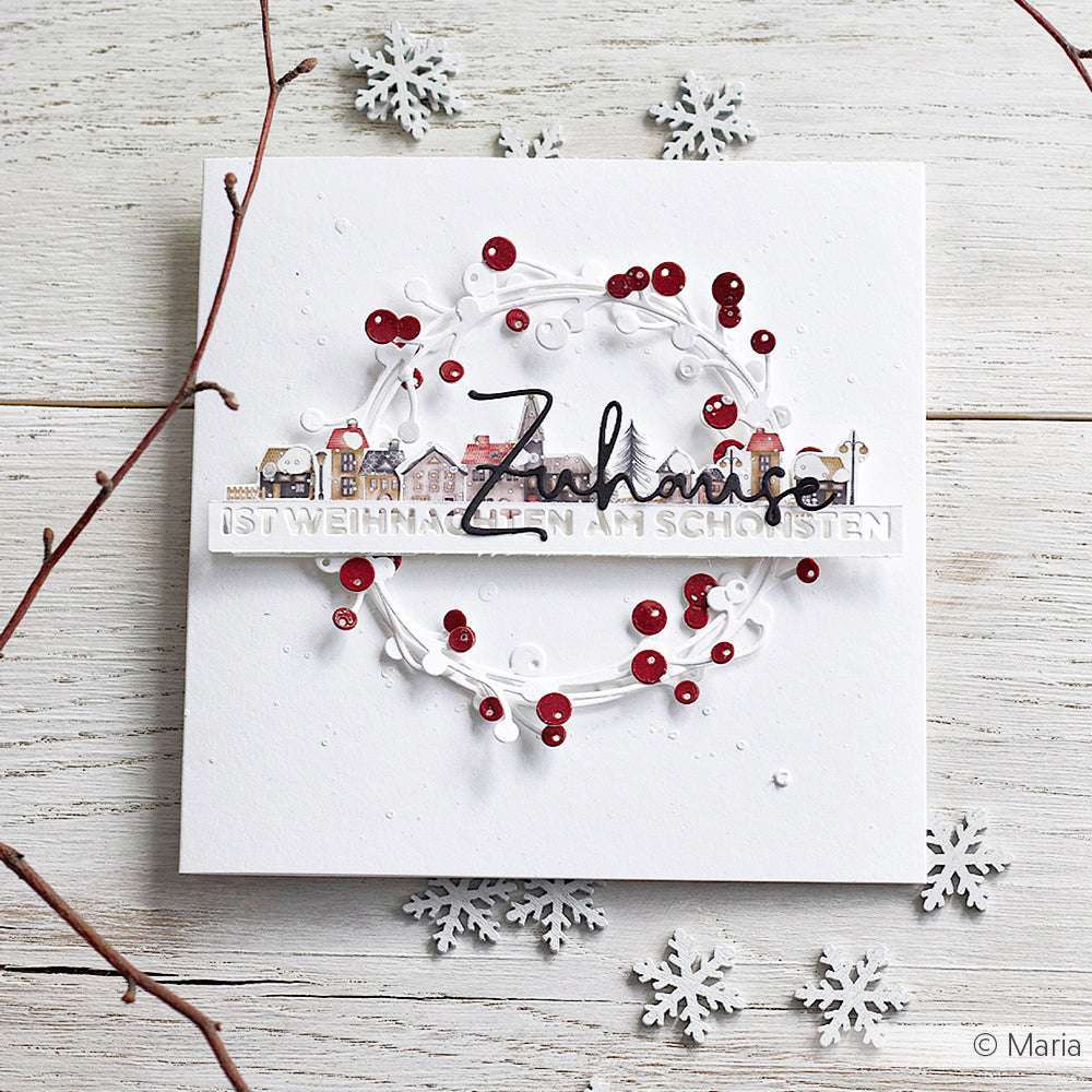 Handgemachte Weihnachtskarte von Alexandra Renke mit einem Kranz, roten Pailletten, einer Dorfszene mit Designpapier und Motivstanze, akzentuiert mit Schneeflocken.