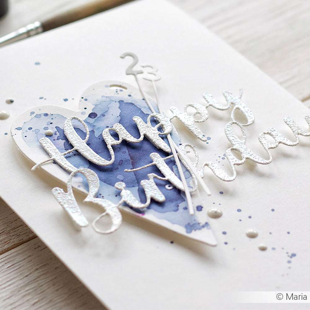 Weiße Karte mit erhabenem "Happy Birthday"-Text über einem blauen Aquarellherz und Farbspritzer-Akzenten, hergestellt mit Alexandra Renke DieCut Systemen für scharfe Kanten und Designpapier Stanzen für einzigartige Textur.