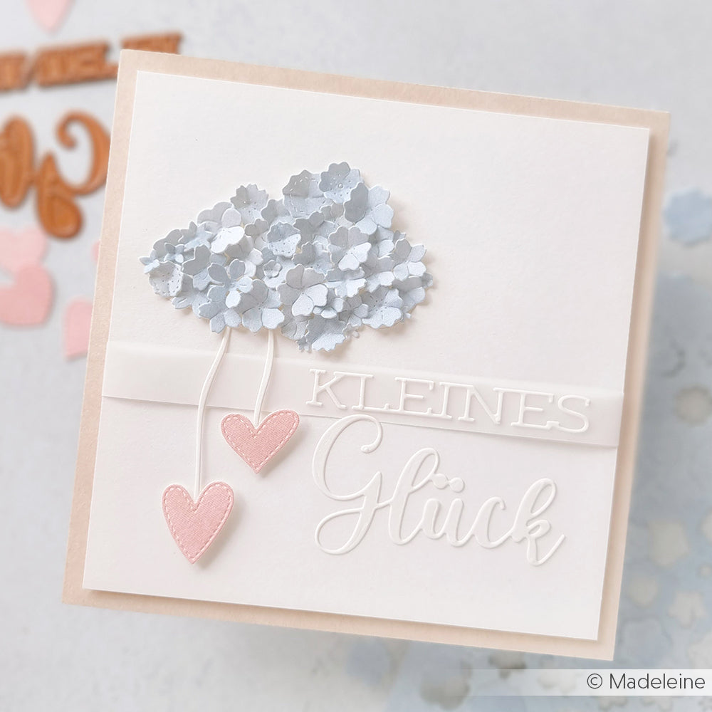 Handgefertigte Karte von Alexandra Renke mit einem blauen Blumenstrauß, zwei rosa Herzen und dem deutschen Text "Schriften-Duo Kleines Glück" auf Weiß. Veredelt mit Motivstanze für dekorative Details.