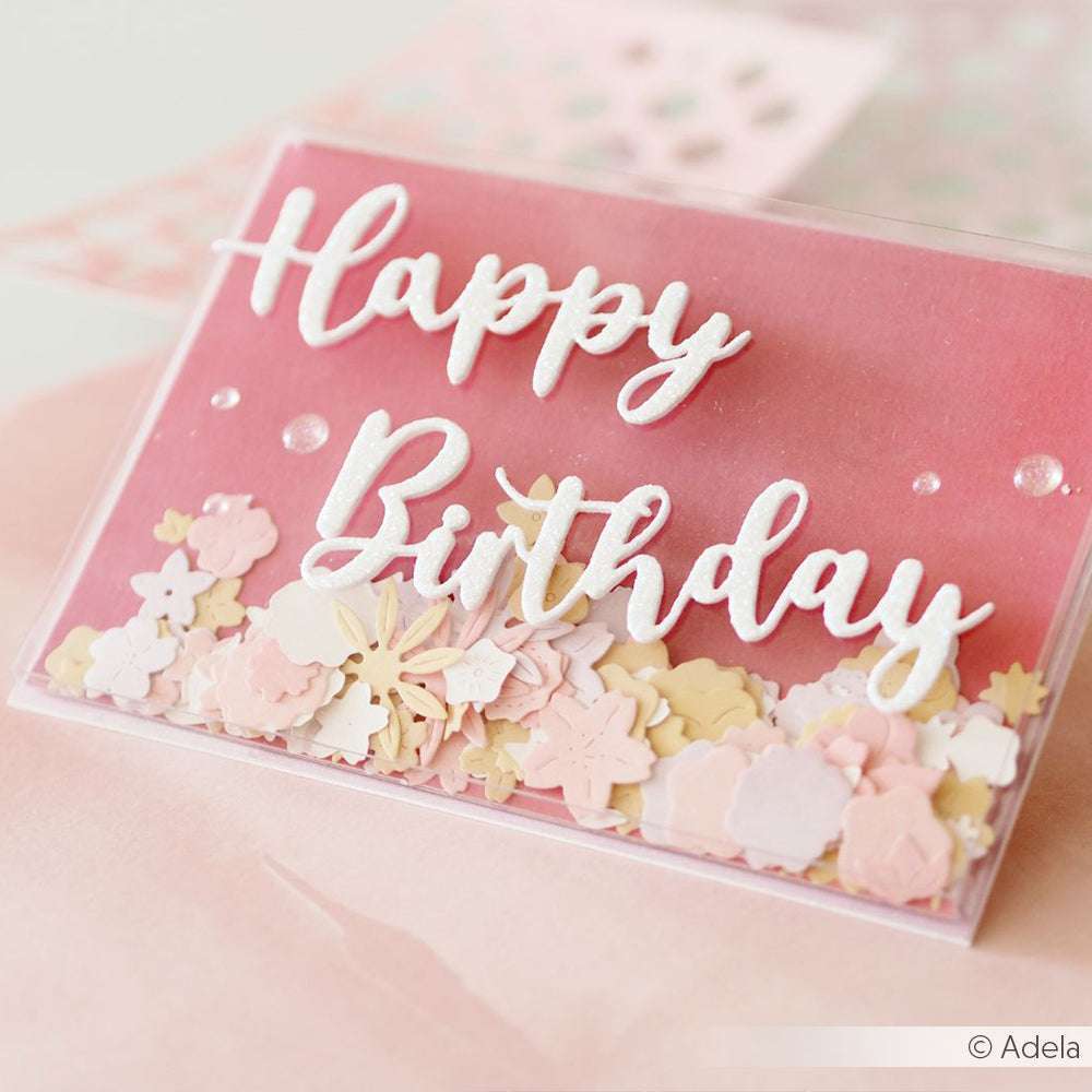 Eine rosafarbene "Happy Birthday"-Karte mit weißer Schrift und pastellfarbenem Blumenkonfetti, hergestellt mit Alexandra Renke Happy Birthday Stanzformen und Stanzsystemen für ein präzises, elegantes Finish.