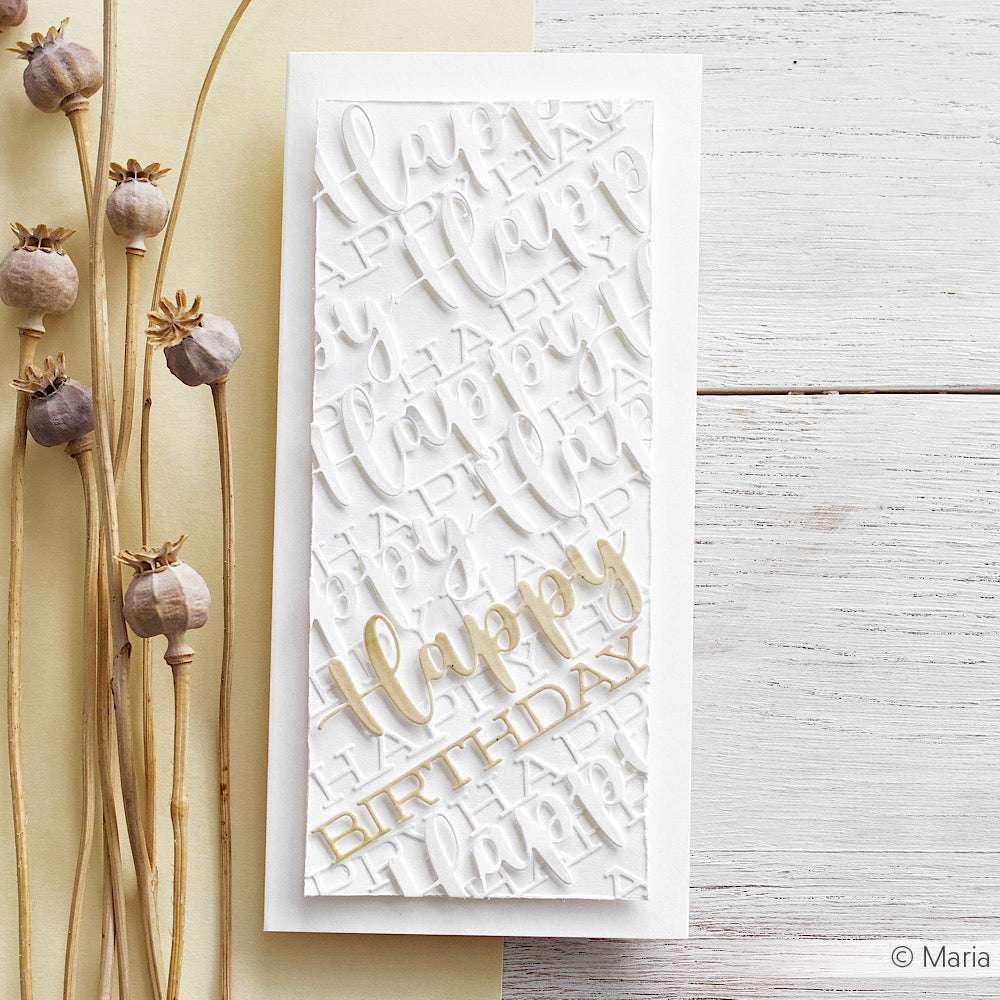 Eine weiße Geburtstagskarte von Alexandra Renke im Schriften-Duo-Design mit geprägtem "Happy"-Text und goldenem "Happy BIRTHDAY" aus einer Motivstanze Happy Birthday, die neben getrockneten Mohnstängeln steht.