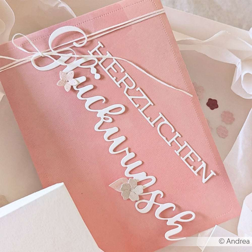 Rosafarbene Karte von Alexandra Renke mit weißem Ausschnitt "Herzlichen Glückwunsch" in der Schriftart Schriften-Duo und mit kleinen Papierblumen verziert.