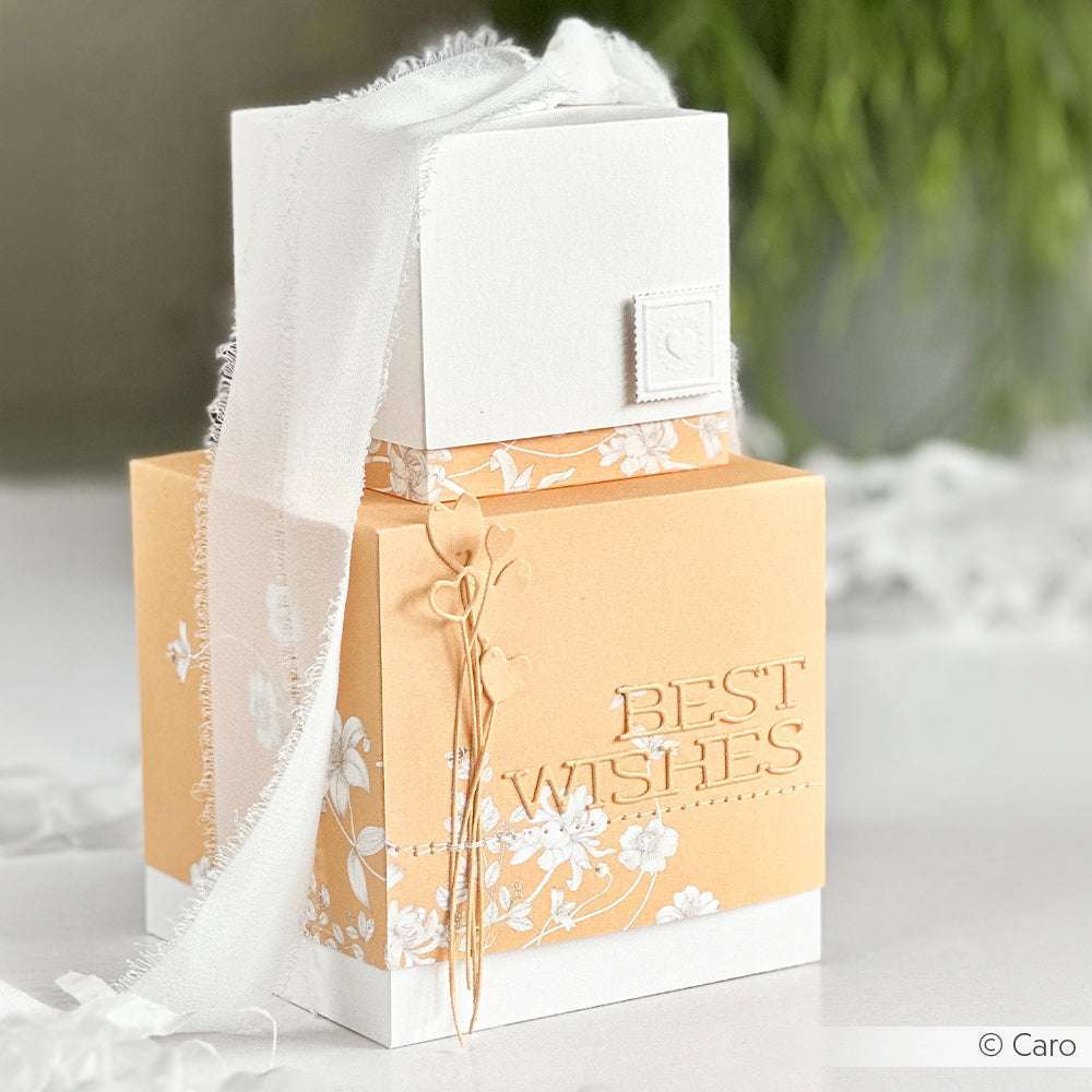 Pfirsichfarbene und weiße Alexandra Renke Geschenkbox mit Schriften-Duo Best Wishes Text, Schleife und floralen Mustern aus Designpapieren, dargestellt auf einer weißen Oberfläche.