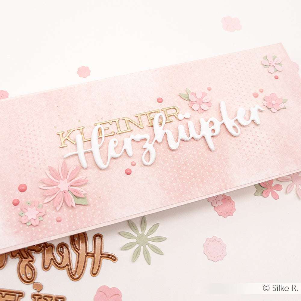 Eine rosafarbene, handgefertigte Karte von Alexandra Renke, die mit Designpapieren, floralen Akzenten und "Kleiner Herzlufer" auf der Vorderseite mit dem Motivstanze Schriften-Duo für elegante Details gestaltet wurde.