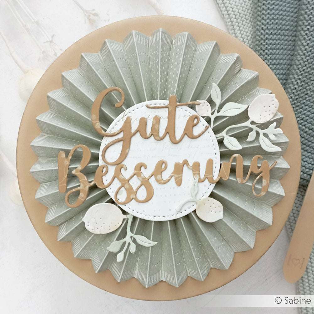 Runde Karte mit gefaltetem grünem Papier, weißen Blumen und "Gute Besserung" in brauner Schrift - gestaltet mit dem Motivstanze Schriften-Duo Gute Besserung von Alexandra Renke für eine herzliche Note.