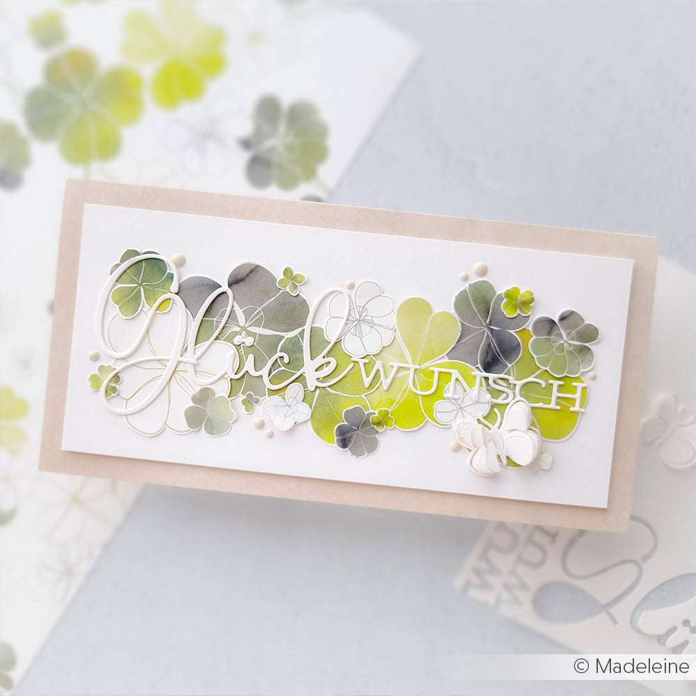 Alexandra Renke Grußkarte mit grünen und grauen Kleeblättern, gestaltet mit der Motivstanze Glück, und "Glückwunsch" in eleganter Schrift.