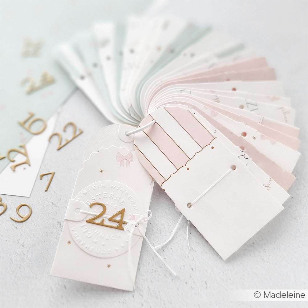 Ein Set von pastellfarbenen nummerierten Anhängern von Alexandra Renke, hergestellt mit der Motivstanze Kleine Serifenzahlen, aufgefächert und mit einer weißen Schnur zusammengehalten.