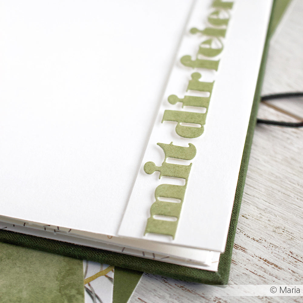 Nahaufnahme einer weißen Karte mit erhabenem grünem Text "mit dir feiern" am Rand, hergestellt mit Alexandra Renke Motivstanze Wörterset, die auf einer grünen Fläche liegt.