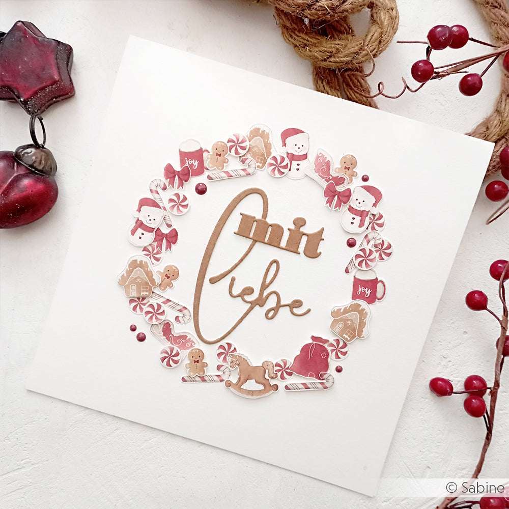 Handgemachte Weihnachtskarte von Alexandra Renke mit einem festlichen Kranz, Lebkuchen, Weihnachtsmann und Zuckerstangen. Der Schriftzug "Mit Liebe" in der Mitte ist mit einem Motivstanze Wörterset oder Stanzen für Papier für zusätzlichen Charme gestaltet.