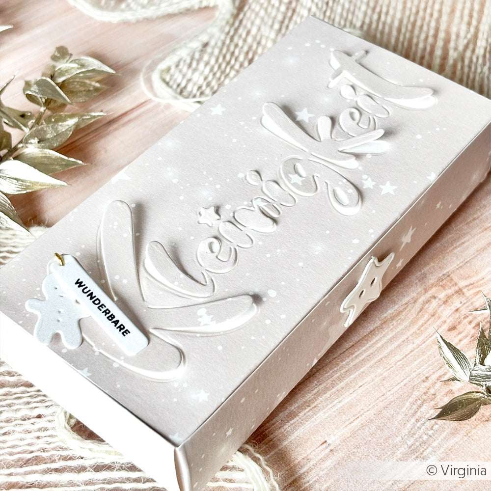 Hochwertige weiße Geschenkbox von Alexandra Renke aus edlem Papier mit dem Schriftzug "Kleinigkeit" in erhabener Schrift, mit dem Kleinigkeit-Stanzwerkzeug gestanzten Sternmotiven und einem kleinen Anhänger mit der Aufschrift "WUNDERBARE".