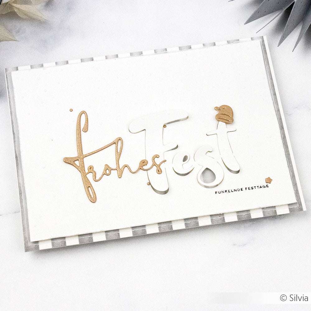 Grußkarte von Alexandra Renke mit "Frohes Fest" in goldener und weißer Schrift auf einem gestreiften Hintergrund mit weihnachtlichen Akzenten - hergestellt mit Motivstanze Wörterset und Stanzsystemen für ein einzigartiges Design.