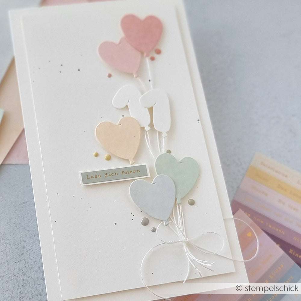 Handgemachte Karte von Alexandra Renke mit pastellfarbenen herzförmigen Luftballons, die mit Deep Edge Motivstanzen hergestellt wurden, und der deutschen Botschaft "Lass dich feiern" auf weißem Hintergrund.