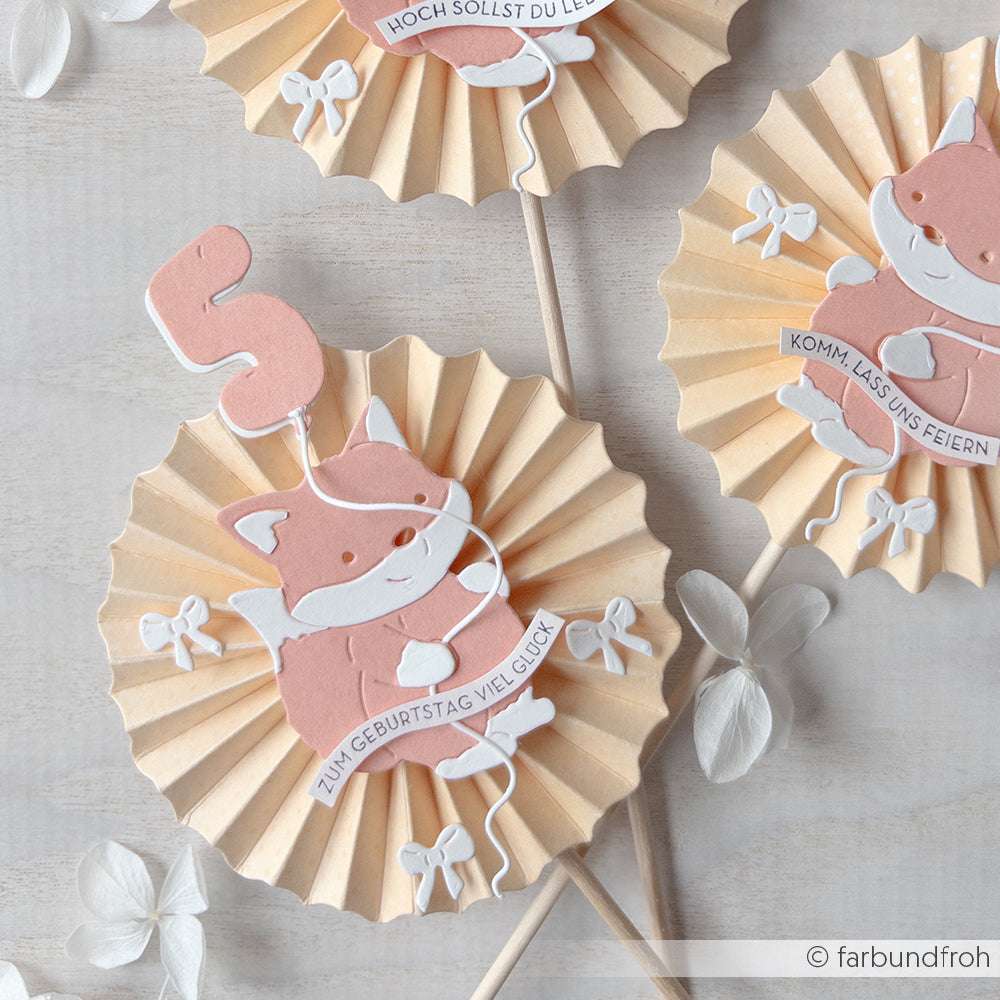 Papierrosetten mit charmanten Fuchs- und Luftballonausschnitten, die jeweils deutsche Geburtstagsgrüße auf Holzstäben zeigen, hergestellt mit Alexandra Renke Motivstanze Ballon-Zahlen für zusätzliches Flair.