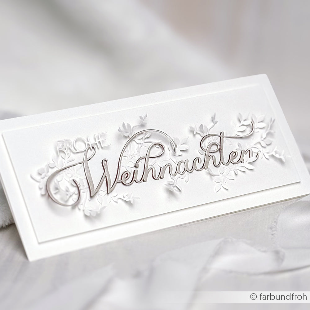 Weiße Karte mit erhabenem Blumendesign, hergestellt mit Alexandra Renke Motivstanze Weihnachten Dies und Stanzsystemen, mit silbernem Text in Schreibschrift "Frohe Weihnachten" auf der Vorderseite.