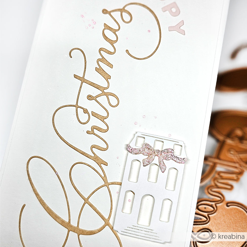 Weiße Karte von Alexandra Renke mit goldener kalligrafischer Weihnachtsschrift, einem kleinen weißen Haus und einer rosafarbenen Glitzerschleife - ideal zum Kombinieren mit Ihren Lieblingsdesignpapieren für festliches Flair.