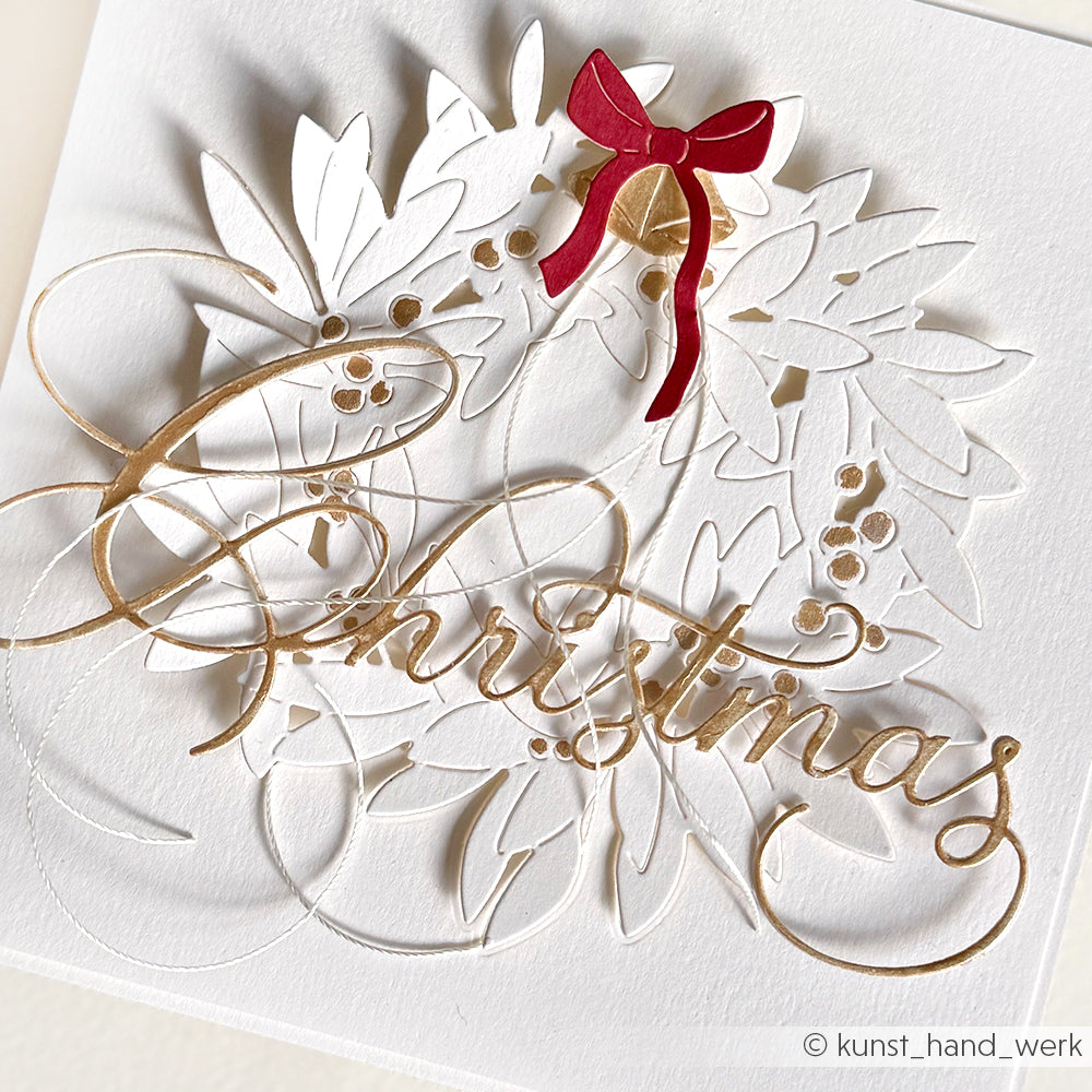 Weiße Karte mit goldenem Weihnachtsschriftzug, weißen Blättern, goldenen Beeren und einer roten Schleife - gestaltet mit Alexandra Renke Designpapieren und Motivstanze Kalligrafisch Christmas für festliches Flair.