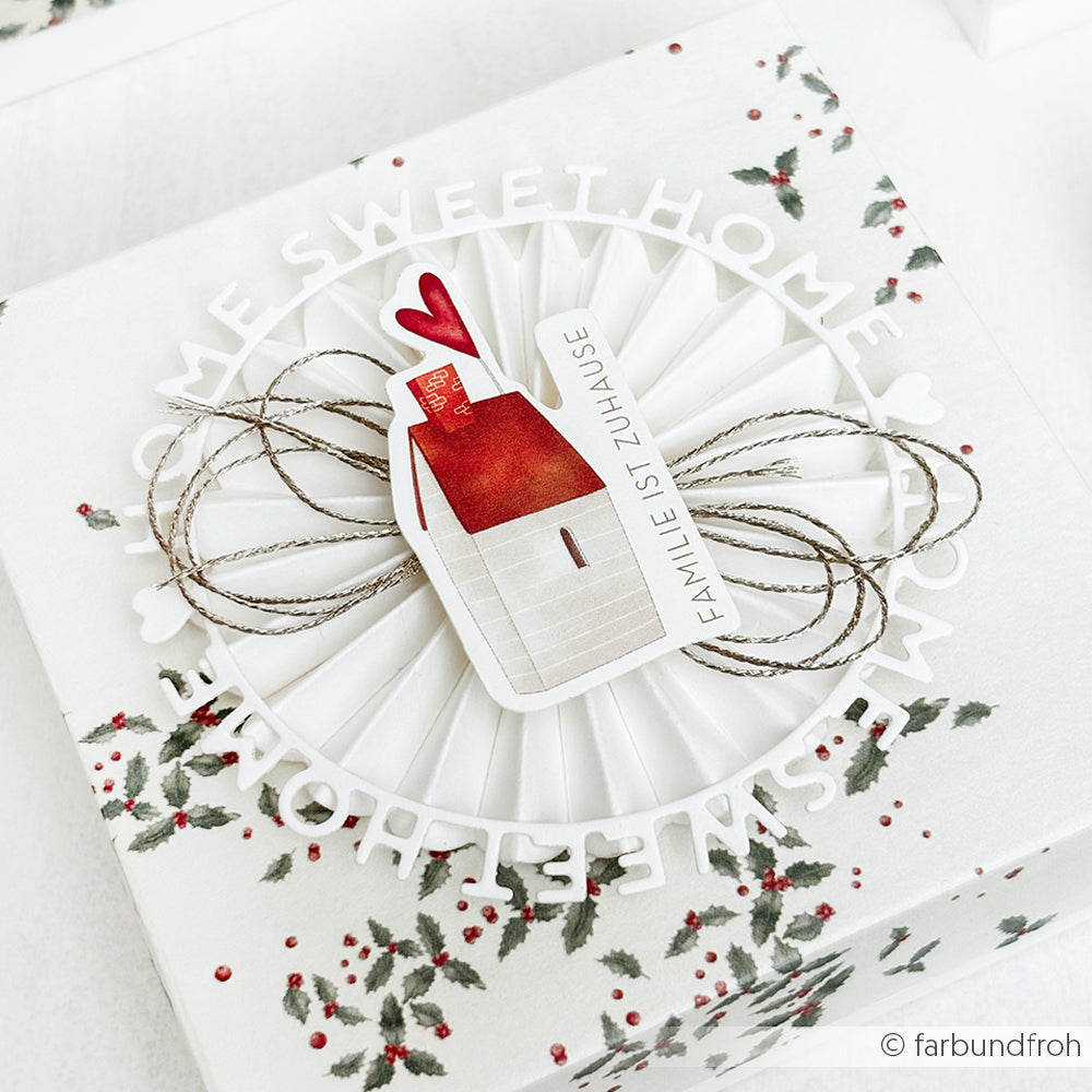Das Geschenk wurde in weißes Papier mit Stechpalmenaufdruck verpackt und mit einem Alexandra Renke "Home sweet home" Typo Kreis Anhänger mit einer Hausillustration aus Motivstanze Dies versehen.