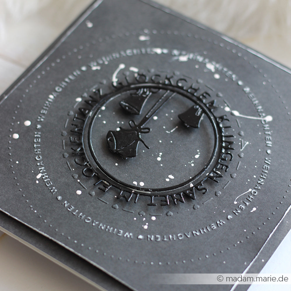 Quadratische schwarze Grußkarte von Alexandra Renke, hergestellt mit DieCut Systemen und geprägten Glöckchen, mit Motivstanze Glöckchen klingen Typo Kreis auf Deutsch, veredelt mit weißen Farbspritzern.