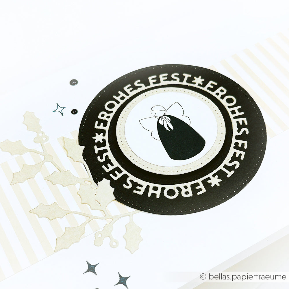 Runde Weihnachtskarte von Alexandra Renke mit dem Text "Frohes Fest" und der Engelsillustration, gestaltet mit Motivstanze Frohes Fest und Stanzen für Designpapier, verziert mit Stechpalmenblättern für einen festlichen Akzent.