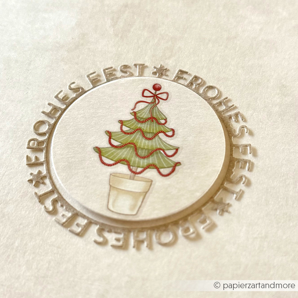 Ein runder Sticker von Alexandra Renke aus Designpapieren zeigt einen Weihnachtsbaum mit dem umlaufend geprägten Schriftzug FROHES FEST" auf weißem Papier.