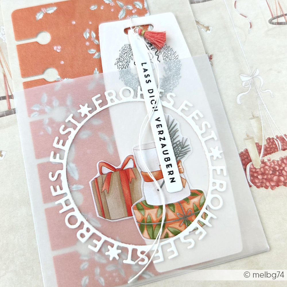 Weihnachtsgeschenkanhänger von Alexandra Renke mit dem Text "Motivstanze Frohes Fest", Geschenken und festlicher Dekoration in einem durchsichtigen Umschlag auf einem weihnachtlichen Hintergrund mit eleganten Designpapieren.