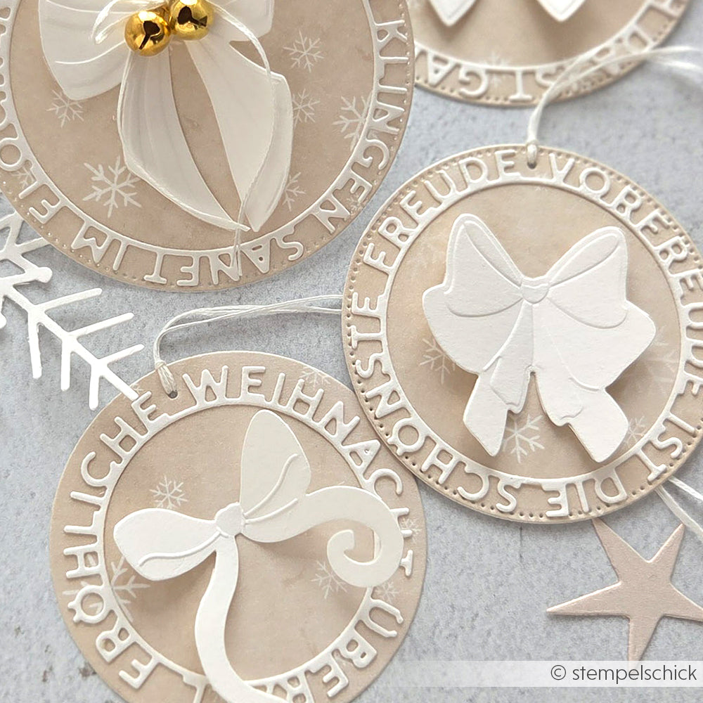 Runde, beigefarbene Weihnachtsanhänger von Alexandra Renke, hergestellt mit DieCut Systeme. Sie sind mit weißen Schleifen, deutschen Weihnachtsgrüßen und Schneeflockenakzenten versehen.