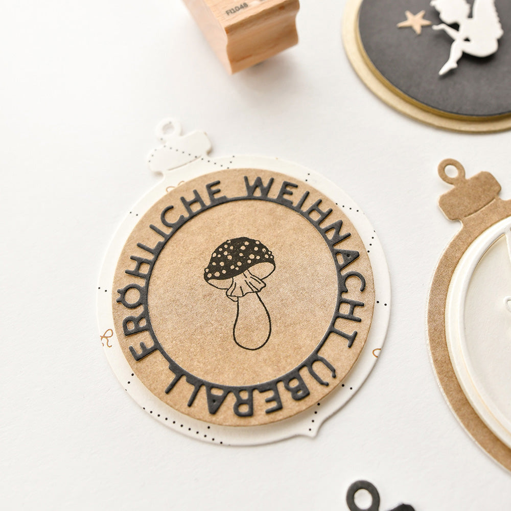 Rundes Papierornament von Alexandra Renke mit einer Pilzzeichnung, hergestellt aus eleganten Designpapieren, mit dem deutschen Text "Fröhliche Weihnachten überall.