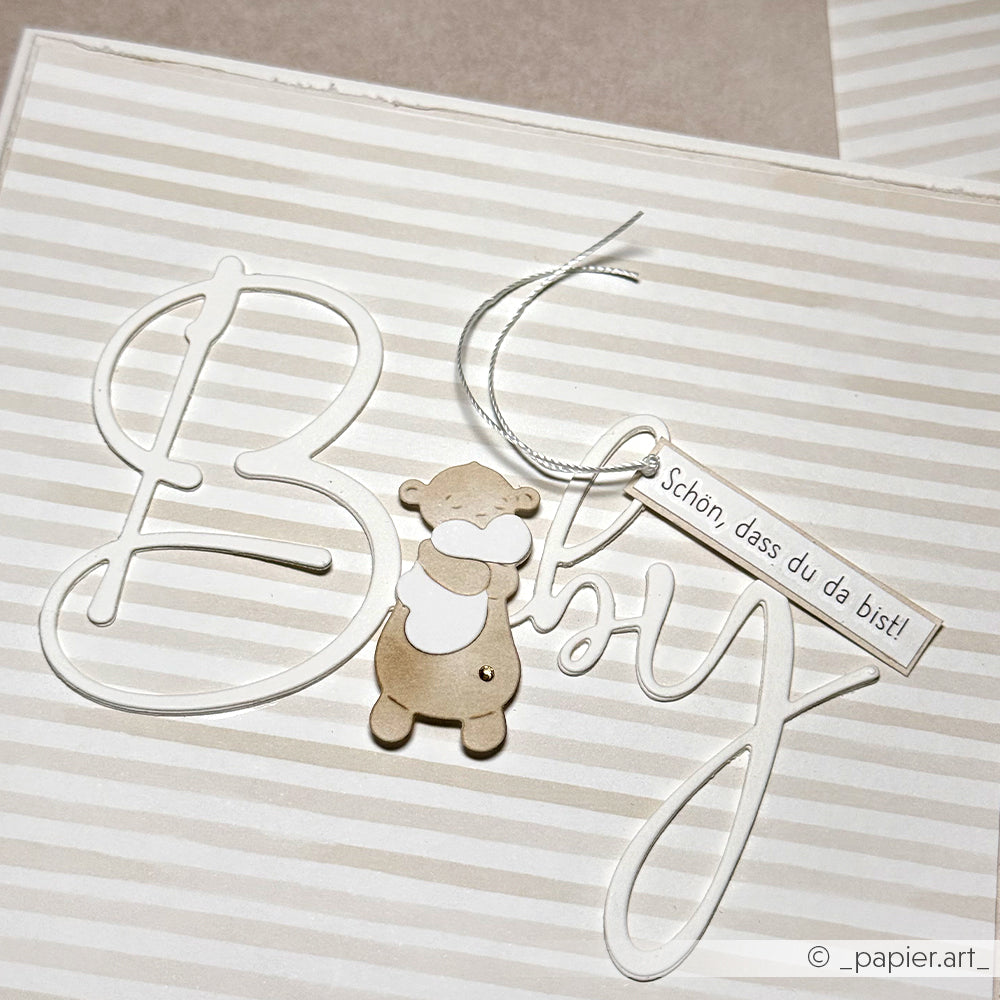 Grußkarte von Alexandra Renke mit dem Schriftzug "Baby", einem kleinen Bären aus der Motivstanze und einem Anhänger mit "Schön, dass du da bist!".